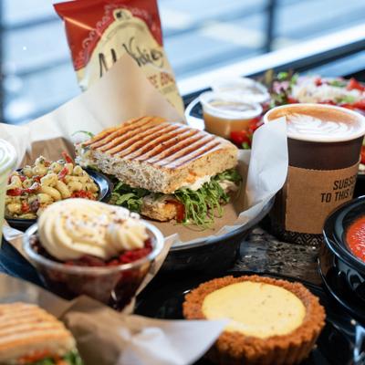 Assorted café meals with panini, pasta salad, coffee, tart.