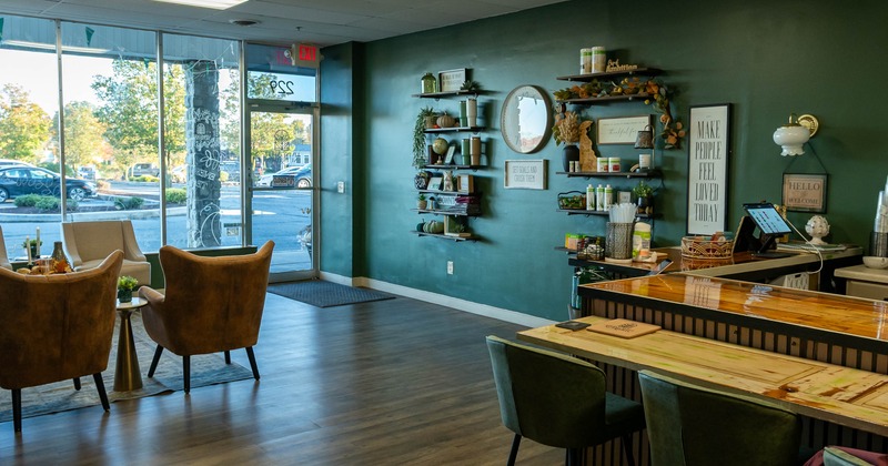 Modern interior - large windows, suede armchairs, green wall with shelves and a wooden counter