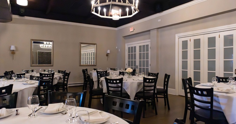 Softly lit restaurant tables set with wine glasses, white plates, and table lamps