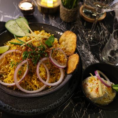 Biryani garnished with sliced red onions, a lemon or lime wedge, cucumber, and herbs.