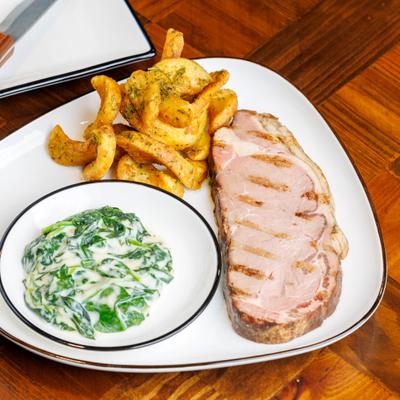 Grilled pork chop served with seasoned potato wedges and creamed spinach.