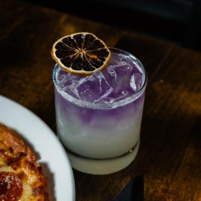 A purple lemonade cocktail topped with a dry lemon wheel.