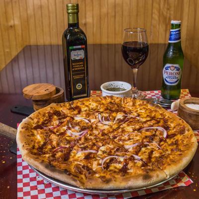BBQ chicken pizza topped with bacon and red onions, accompanied by drinks and condiments.