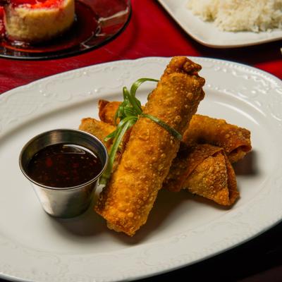 Fried egg rolls served with a side of dark dipping sauce.