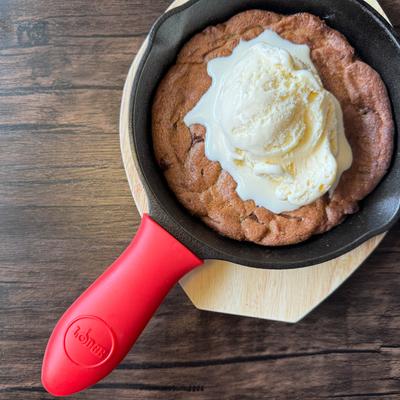 Chocolate chip cookie in a skillet pan with red handle and vanilla ice cream on top.