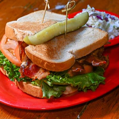 BLT sandwich served with a pickle and coleslaw on the side.
