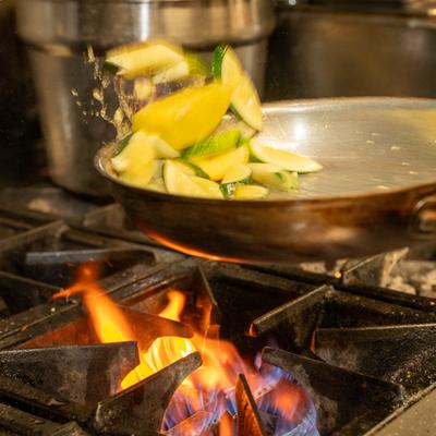 Vegetables being sauteed in a stainless steel skillet over a high-heat gas stove.