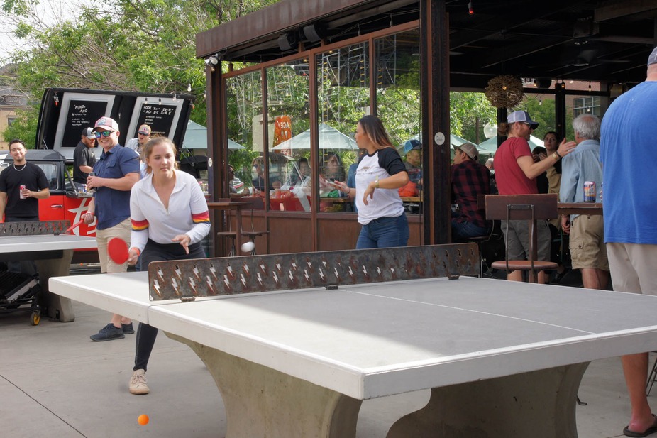 A pair of guests playing ping pong outside, with people in the background.