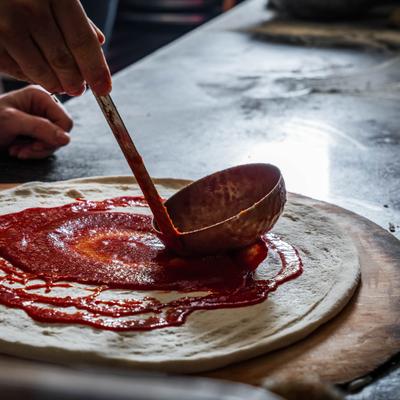 Staff member spreading tomato sauce on a pizza dough.