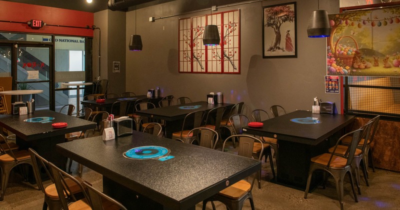 Interior of a modern restaurant with dark tables, metal chairs and decorative wall art
