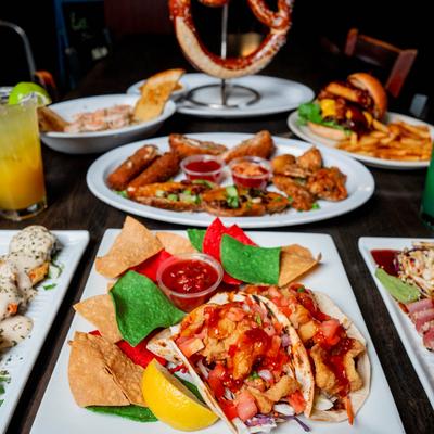 Vibrant food spread with tacos, appetizers, burger, pretzel, and cocktails.