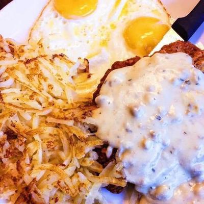 Chicken fried steak with white gravy, hash browns and two sunny side eggs, top view.