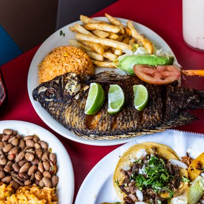 Whole fried fish topped with lime wedges, served alongside rice, fries, and beans.