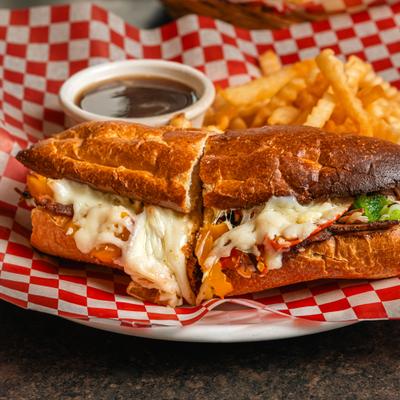 Steak philly sandwich served with fries and dipping sauce on a plate.