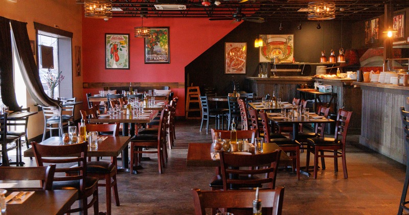 Interior of a restaurant with wooden tables and chairs, decorated with vintage posters and warm lighting