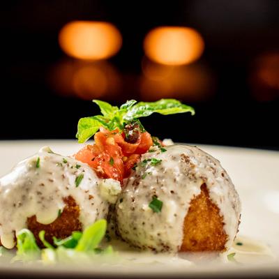 Two croquettes topped with creamy sauce, diced tomato, and basil garnish.