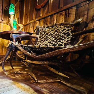Rustic antler chair beside a wooden table and a green lamp in a wooden interior.