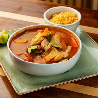 Bowl of hearty Mexican seafood stew accompanied by a side of rice and lime wedges.
