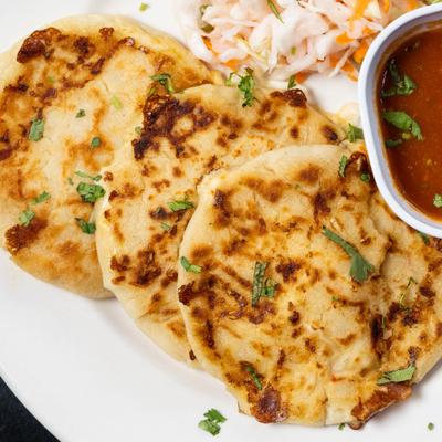 Round grilled tortillas topped with herbs beside slaw and salsa.