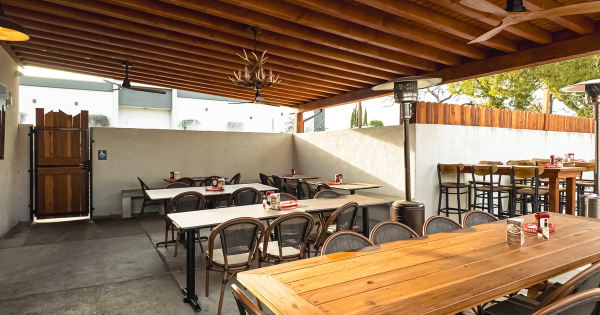 Outdoor dining area with tables, chairs, and ceiling fans under a wooden pergola