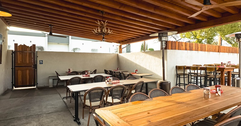 Outdoor dining area with tables, chairs, and ceiling fans under a wooden pergola