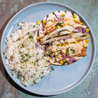 Fried Fish Tacos topped with a creamy sauce and served with a side of white rice.