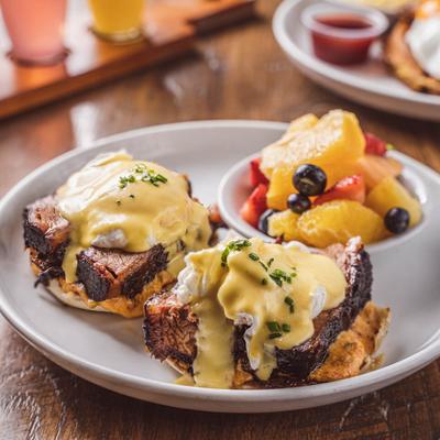Brisket eggs Benedict with hollandaise sauce and a cup of fruit