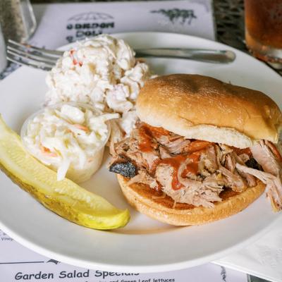 Barbecue pork sandwich served with potato salad, coleslaw and pickle.
