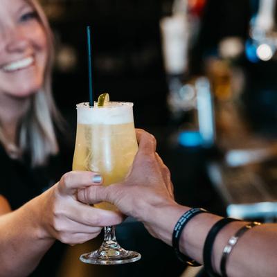 A bartender handing a frothy cocktail to a patron at the bar