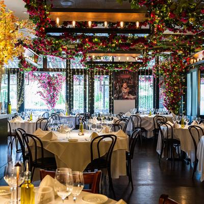 Dining area, fully set round tables, hanging floral decorations.
