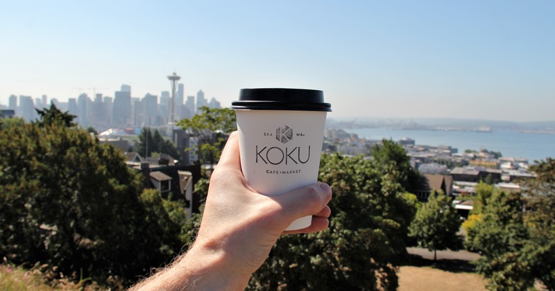A coffee cup held in the air with the city and bay view in the background