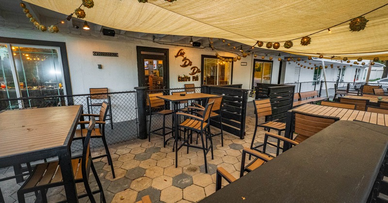 Outdoor patio dining area with wooden tables and chairs, canopy and string lights
