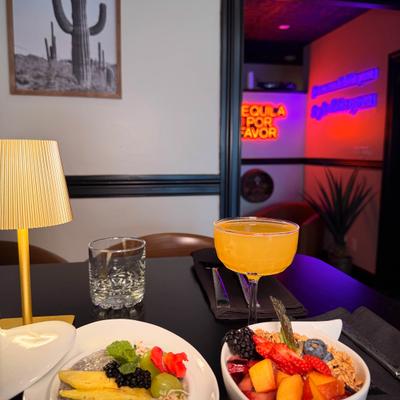 Breakfast table with fruit bowl, orange cocktail, water glass, and a lamp.