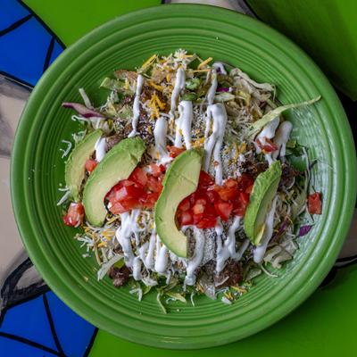 Colorful salad with avocado, tomato, cheese, and sour cream on a green plate.