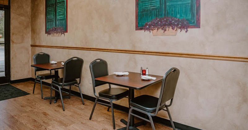 Restaurant interior with two tables and chairs against a beige wall with green shutter murals.