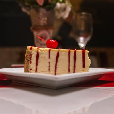 Cheesecake slice topped with berry sauce and a maraschino cherry.