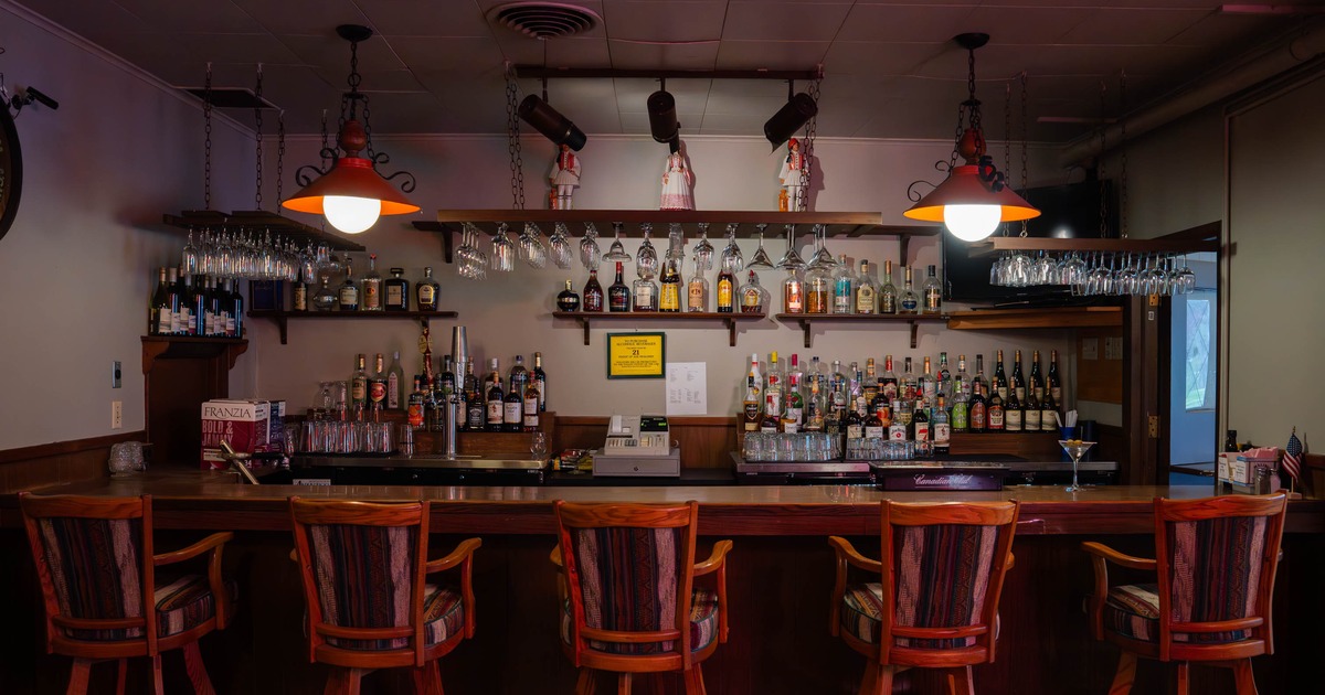 A cozy, well-stocked bar with wooden stools and warm lighting.