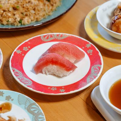 Tuna nigiri on red patterned sushi plate, surrounded by various other dishes.