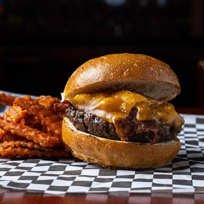 Bacon Cheeseburger served alongside seasoned fries on a checkered paper liner.