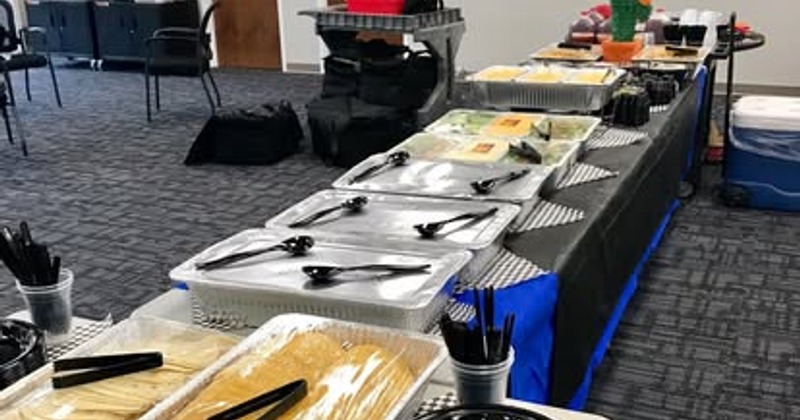 Catered buffet setup with foil pans on a long table covered with a black tablecloth