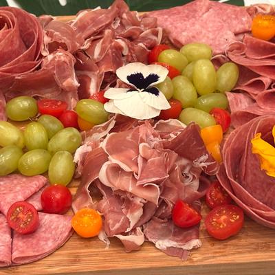 Charcuterie platter with cured meats, grapes, cherry tomatoes, and flower garnish.