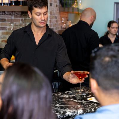 Bartender in a black shirt placing down a cocktail at the bar.
