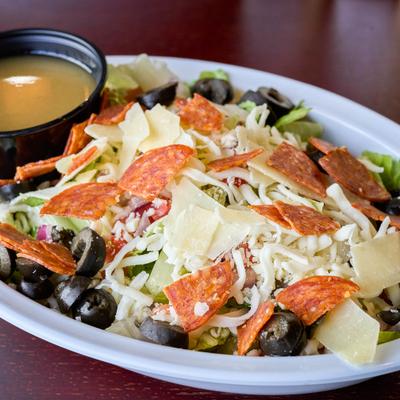 Italian salad with pepperoni, olives, cheese, and a cup of dressing.