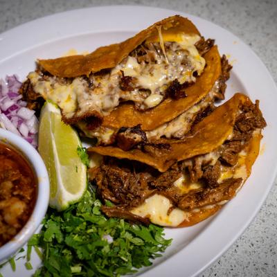 Quesabirria tacos served with lime, cilantro, onion, and consommé.