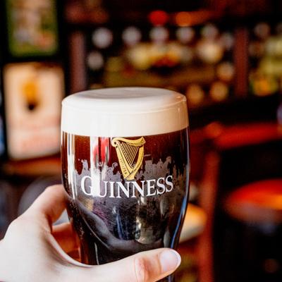 A hand holds a pint of Irish dry stout in a bar setting.