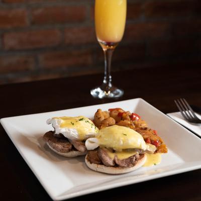 Eggs Benedict with a side of potatoes and an orange drink.