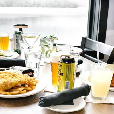 A table by a window set with multiple food plates, beer, cocktails, and glasses of water.