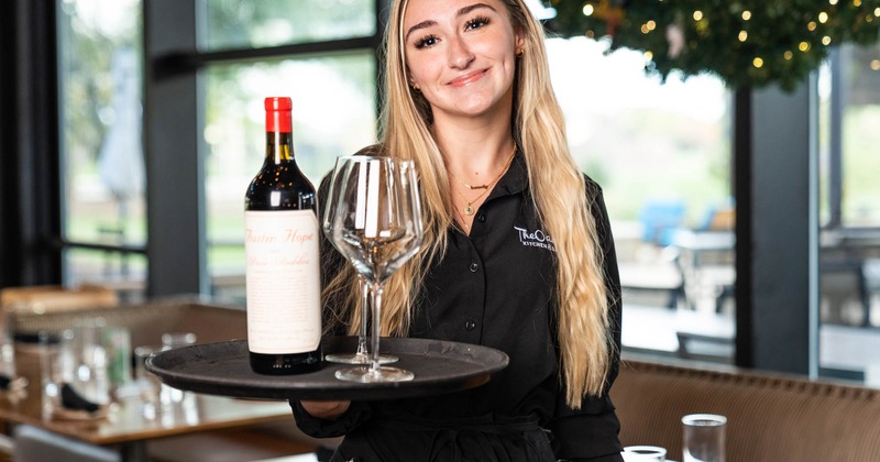 A wine server holding a tray with a bottle of wine and a glass on it