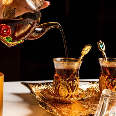 Tea being poured into an ornate glass cup on a decorative gold tray.