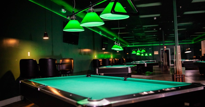 Interior, pool tables, green lighting, chairs, tables